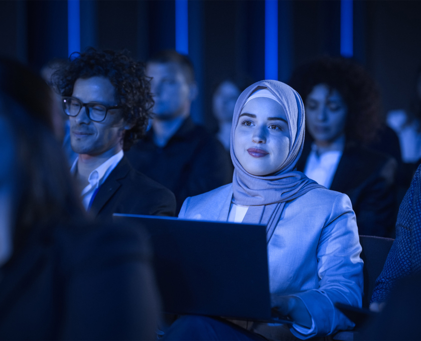 Front View Of A Woman In Panel Audience Taking Notes On Her Laptop